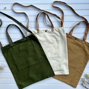 May include: Three canvas tote bags with long straps. The bags are in green, beige, and white.