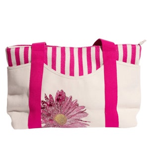 May include: A white canvas tote bag with pink stripes and a pink flower design. The bag has two pink handles.