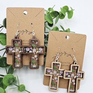 May include: A pair of wooden cross earrings with a floral design. The earrings are on a brown card with the text "Southern Joy Creations".