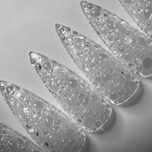 May include: Five clear glass ornaments shaped like cones with a textured surface. The ornaments have a pattern of small bubbles.