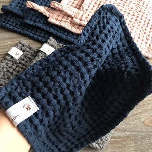 May include: A set of blue, gray, and pink waffle weave kitchen towels with a small brown label that says "The Little" on it.