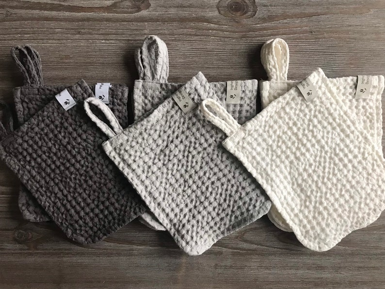 May include: Five waffle weave kitchen towels in different colors: gray, light gray, white, dark gray, and black. Each towel has a loop handle and a small tag with the text "Hand Made" on it.