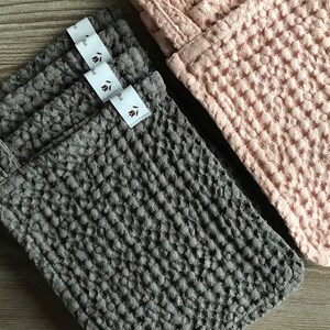 May include: Four gray waffle weave kitchen cloths with a hanging loop and a white label that says "leaf" stacked on top of each other. A pink waffle weave kitchen cloth is visible in the background.