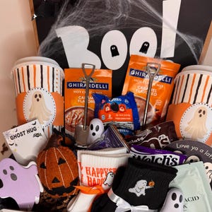 以下が含まれることがあります： ハロウィーンをテーマにしたギフトボックス。ストライプ柄の紙コップ2個（ゴーストのデカール付き）、ギラデリのキャラメルホットココアミックス、オレオ、フェルト製のカボチャ、ゴースト柄の靴下、ゴースト型のカード、小さなゴーストのフィギュアが入っています。