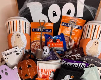 May include: A Halloween-themed gift box containing two striped paper cups with ghost decals, Ghirardelli caramel hot cocoa mix, Oreo cookies, a felt pumpkin, white and black socks with ghost motifs, a ghost-shaped card, and small ghost figurines.