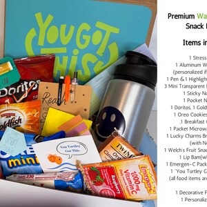 May include: A gift box filled with snacks, a water bottle, and stationery. The box includes chips, cookies, a stress ball, a water bottle with a smiley face, pens, highlighters, and a card that says "You Got This".