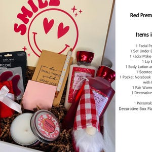 May include: A red premium gift box filled with self-care items. Includes a facial peel mask, under eye patches, lip balm, body lotion, a scented candle, a notebook, socks, and a decorative gnome. The box has a smiley face design.