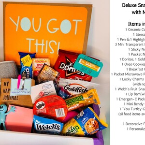 May include: A deluxe snack box with a mug, filled with various snacks, a ceramic coffee cup, and a stress ball. The box includes a notepad, highlighter tabs, and a small figurine. The box has the words "YOU GOT THIS!" on the back.