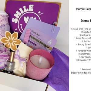 May include: A purple gift box filled with self-care items. Includes a coffee cup with butterfly design, candle, hand mask, nail polish, and a wooden flower. The box has the word "SMILE" on a purple background.