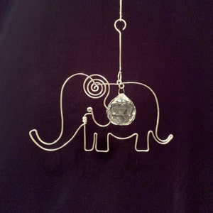 May include: A silver wire elephant sculpture with a clear crystal ball hanging from it. The elephant is suspended from a silver hook.
