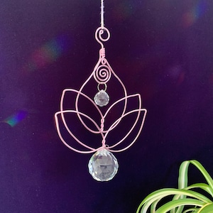 May include: A pink wire crystal suncatcher with a lotus flower design and two clear crystal prisms hanging from it.