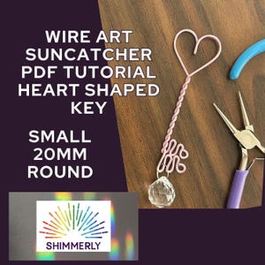 May include: A pink wire art suncatcher in the shape of a key with a heart-shaped top and a crystal pendant. The image includes text that reads "WIRE ART SUNCATCHER PDF TUTORIAL HEART SHAPED KEY SMALL 20MM ROUND" and the logo for "SHIMMERLY".