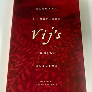 May include: A cookbook titled "Vij's Indian Cuisine" with a deep red cover and white text. The cover features the words "Elegant & Inspired" and "Indian Cuisine". The author's names, Vikram Vij and Meeru Dhalwala, are also listed.