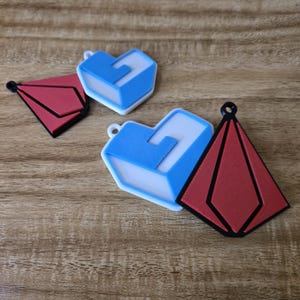 May include: Two heart-shaped and two geometric charms. The heart charms are blue with white accents, and the geometric charms are red with black outlines. Each charm has a small loop for hanging.