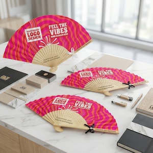 Peut inclure: Éventails en bois avec un motif ondulé rose et orange vif, avec le texte "FEEL THE VIBES" et "YOUR SLOGAN HERE". Ils sont présentés avec des cartes de visite, des blocs-notes et des clés USB, parfaits pour la promotion.