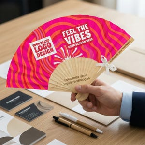 Pode incluir: Um leque rosa e laranja com o texto "FEEL THE VIBES" e "YOUR SLOGAN HERE". O leque tem um cabo de madeira e uma fita branca. O texto "YOUR BRAND LOGO DESIGN" também é visível. O leque está na mão de uma pessoa.