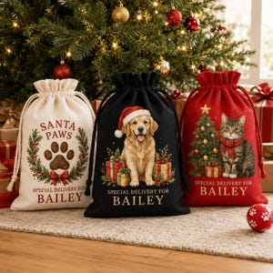 Może przedstawiać: Trzy worki prezentowe ze sznurkiem i świątecznymi wzorami. Kremowy worek przedstawia odcisk łapy oraz napis SANTA PAWS SPECIAL DELIVERY FOR BAILEY. Czarny worek ukazuje golden retrievera w czapce Mikołaja oraz odpowiedni napis.