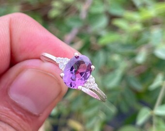 May include: A silver ring with a large oval-shaped purple gemstone and smaller clear gemstones on the band.