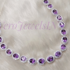 May include: A silver necklace with a row of oval-shaped purple gemstones surrounded by smaller clear gemstones.