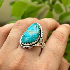 Könnte beinhalten: Ein türkisfarbener Ring mit einer silbernen Fassung. Der Türkis-Stein hat eine Tropfenform und eine blaugrüne Farbe mit braunen Adern.