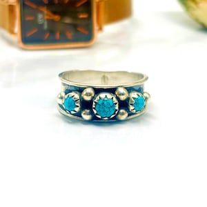 Op de afbeelding: Een zilveren ring met drie turquoise stenen gezet in een band met decoratieve accenten.