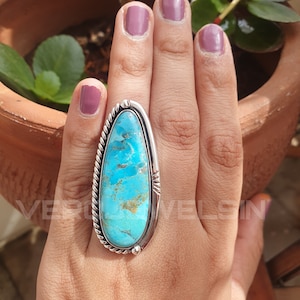 May include: A large, turquoise gemstone ring with a silver setting. The turquoise stone is a vibrant blue-green color with brown matrix patterns. The ring has a rope-like texture around the stone and is set on a hand.