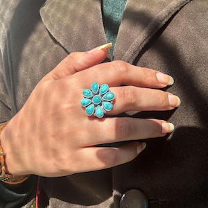 Può includere: Un anello d'argento con un designo a forma di fiore turchese. L'anello ha nove pietre turchesi a forma di fiore.