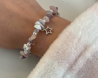 May include: A bracelet made with small, irregular shaped stones in shades of pink and purple. The bracelet has a silver star charm.
