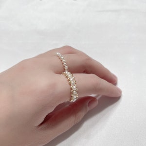 May include: Two gold rings with white pearl beads. The rings are stacked on a finger.