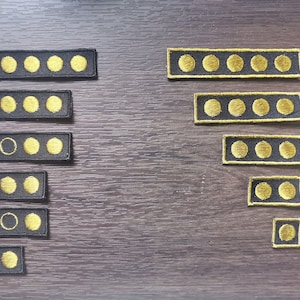 Könnte beinhalten: Ein Satz von neun schwarzen gestickten Patches mit goldenen Kreisen. Die Patches sind in zwei Reihen angeordnet, wobei die größeren Patches oben und die kleineren Patches unten sind. Die Patches sind alle rechteckig und haben einen schwarzen Rand.