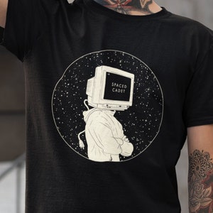 May include: A black t-shirt with a white graphic of a person with a computer monitor for a head. The text on the monitor says "SPACED CADET". The graphic is set against a black background with white stars.