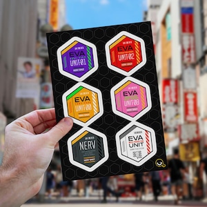 May include: A sheet of hexagonal stickers featuring designs from the anime series, Neon Genesis Evangelion. Each sticker has a unique color scheme and text, including "EVA UNIT-01", "EVA UNIT-02", "EVA UNIT-00", "EVA UNIT-08", "NERV", and "EVA MASS PRODUCTION UNIT".