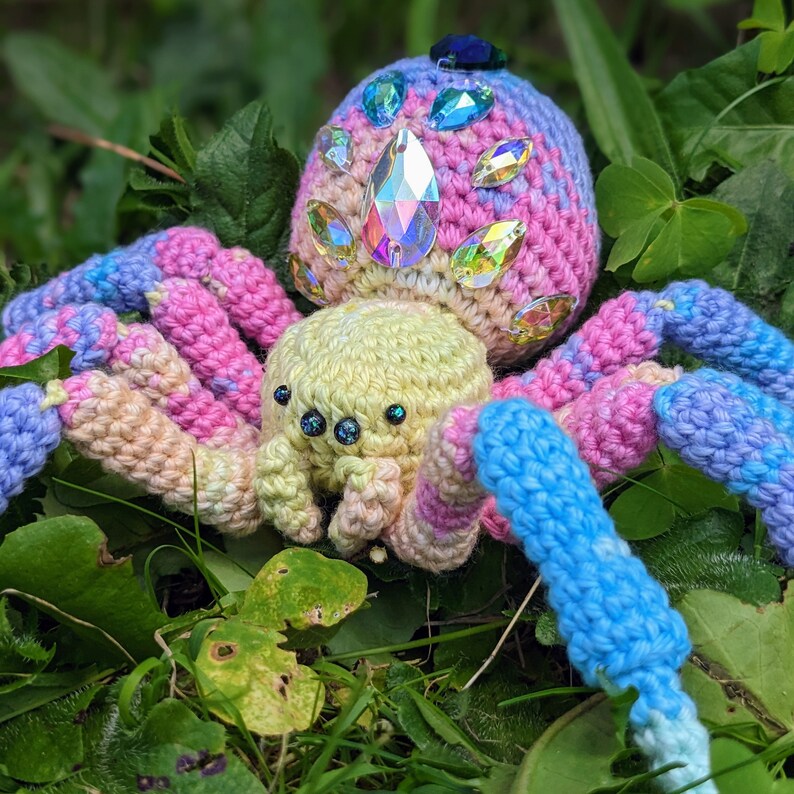 This photo is a close up of a crocheted spider that is rainbow and has crystals on its back