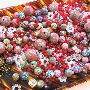 May include: A collection of colorful beads in a variety of shapes and sizes. The beads are made of glass, ceramic, and plastic. They are arranged in a bowl and include red, blue, green, and white beads.