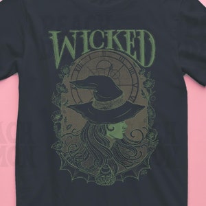 May include: A dark blue t-shirt with a green and brown graphic print of a witch with a hat and long hair. The graphic also includes a clock and floral elements. The text "WICKED" is printed in green above the graphic.