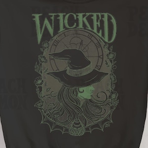 May include: Black sweatshirt with a green graphic print of a witch wearing a hat and holding a clock. The text "WICKED" is printed above the witch.