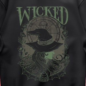 May include: Black sweatshirt with a green graphic print of a witch with a clock and the word "WICKED" above her.