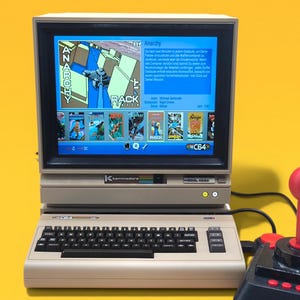 Könnte beinhalten: Ein beigefarbener Vintage-Heimcomputer mit integriertem Monitor, der ein Spielmenü mit dem Titel Anarchy anzeigt. Der Computer verfügt über eine QWERTY-Tastatur und einen schwarzen Bildschirmrand. Rechts daneben steht ein schwarzer Joystick mit rotem Knauf.