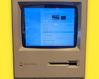 Może przedstawiać: Vintage wyświetlacz komputera Macintosh Plus w beżowej obudowie. Ekran wyświetla niebieski interfejs z różnymi ustawieniami. Widoczne logo Apple. Tekst na dole brzmi: "This offer is for the display only, NOT the Macintosh Computer!"