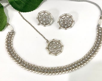 May include: A silver necklace with a pendant and earrings. The necklace and earrings are decorated with white pearls and clear cubic zirconia stones.