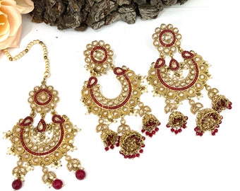 May include: A set of gold-tone earrings and a matching maang tikka, featuring a red and white design with pearl accents. The earrings have a crescent moon shape with dangling bells.