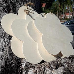 May include: A set of four unfinished wooden flower-shaped ornaments. The ornaments are stacked on top of each other and are hanging from a tree branch.