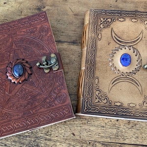 May include: Two leather-bound journals with decorative designs and blue gemstone accents. One journal features a pentacle design and the other features a triple moon design.