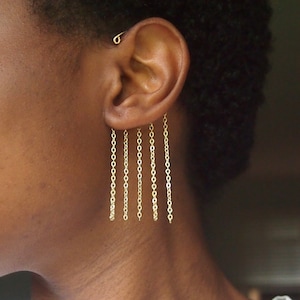 May include: Gold chain earrings featuring multiple hanging strands. The earrings are crafted from fine, delicate gold chains that cascade from the earlobe. The chains are attached to a small stud on the ear. These earrings are a simple yet elegant accessory.