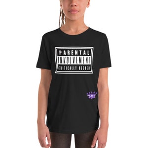 May include: Black youth t-shirt with a white graphic that says "Parental Involvement Critically Needed" in a style similar to a warning label. The graphic is surrounded by a black rectangle. A small purple logo is on the bottom right of the shirt.
