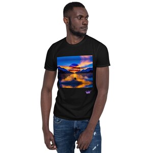 Op de afbeelding: Zwart t-shirt met een levendige landschapsprint. Het ontwerp toont een zonsondergang boven een meer, met bergen op de achtergrond. De afbeelding wordt weerspiegeld in het water, waardoor een symmetrisch effect ontstaat. Een klein logo is rechtsonder zichtbaar.