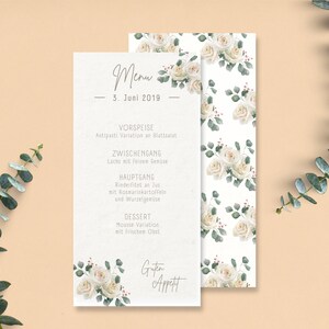 May include: A white menu card with a floral design featuring white roses and green leaves. The menu card lists the courses for a wedding reception: Antipasti Variation, Lachs mit feisen Senize, Rinderfitet an lut, Mousse Variation, and Guten Appett. The date is 3. Juni 2019.