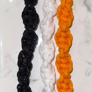 May include: Three keychains with black, white and yellow braided tassels. Each keychain has a silver metal ring and a silver metal clasp.