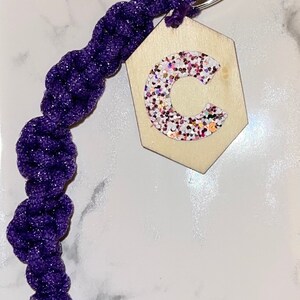May include: Purple and silver keyring with a wooden hexagonal charm featuring a glitter letter C.
