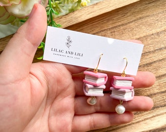 May include: A pair of pink book stack earrings with pearl accents. The earrings are handmade and feature a gold hook.